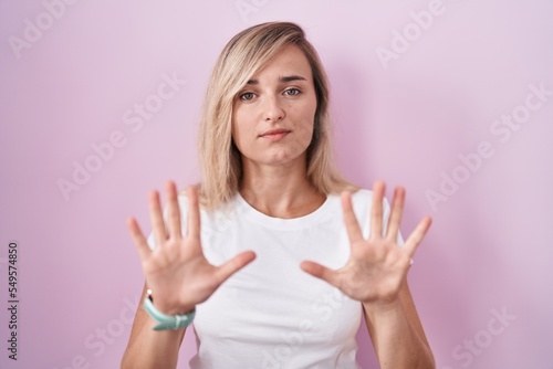 Young blonde woman standing over pink background moving away hands palms showing refusal and denial with afraid and disgusting expression. stop and forbidden. © Krakenimages.com
