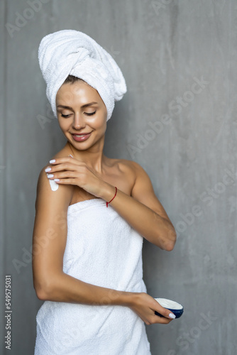Young pretty woman in towel after shower applying a body cream. Skin care.