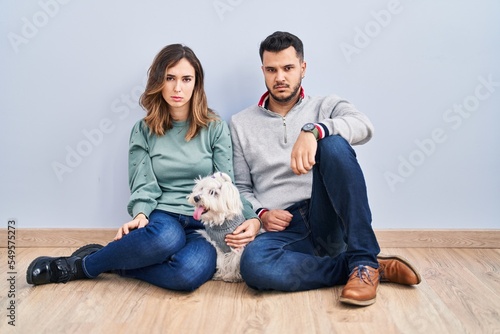 Young hispanic couple sitting on the floor with dog skeptic and nervous, frowning upset because of problem. negative person.