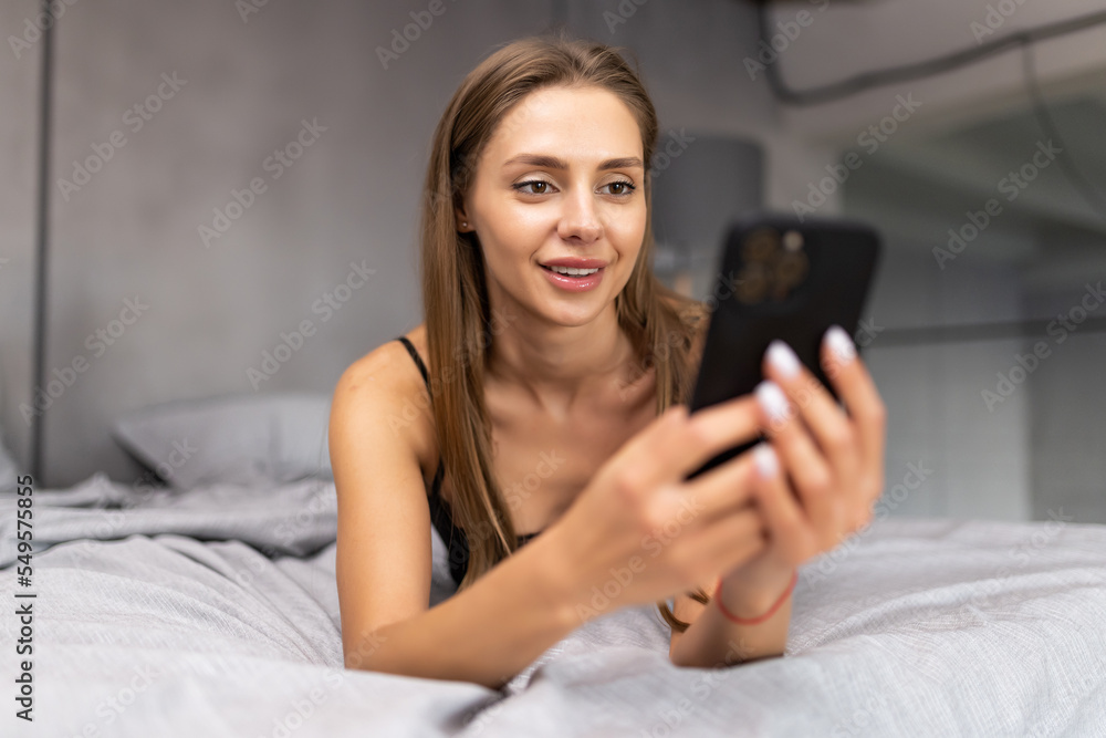 Woman in bed checking social apps with smartphone. Sexy woman making video call, lying on bed in the morning. Woman in bed checking social apps with smartphone. Sexy woman making video call, lying on bed in the morning.