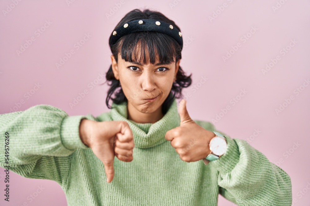 Young beautiful woman standing over pink background doing thumbs up and down, disagreement and agreement expression. crazy conflict Young beautiful woman standing over pink background doing thumbs up and down, disagreement and agreement expression. crazy conflict