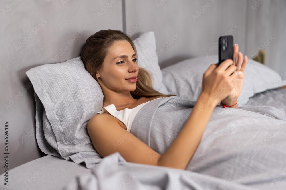 Top view awakened woman lying in bed holds smart phone looks at screen watching time overslept and late feels stressed Top view awakened woman lying in bed holds smart phone looks at screen watching time overslept and late feels stressed