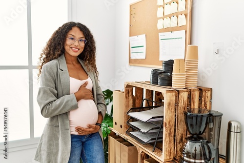 Young latin woman pregnant smiling confident standing at office