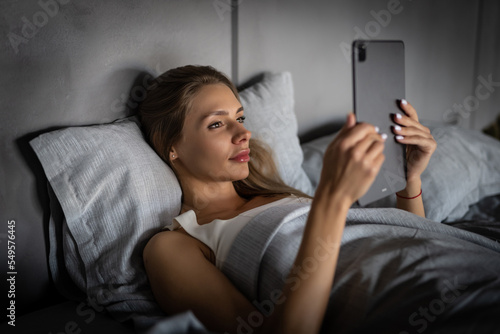 Beauty woman using tablet pc in her bed at night. Beautiful young woman with tablet computer in a dark room