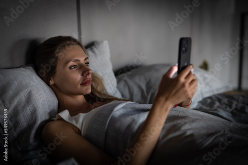 Young woman look at smart phone and lying on bed at night