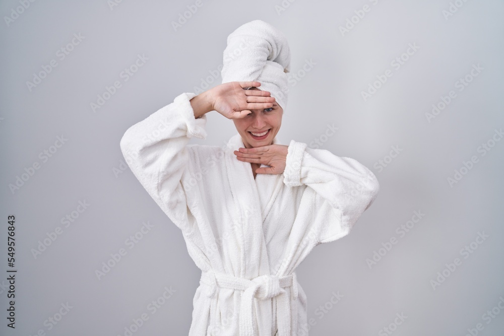 Blonde caucasian woman wearing bathrobe smiling cheerful playing peek a boo with hands showing face. surprised and exited Blonde caucasian woman wearing bathrobe smiling cheerful playing peek a boo with hands showing face. surprised and exited