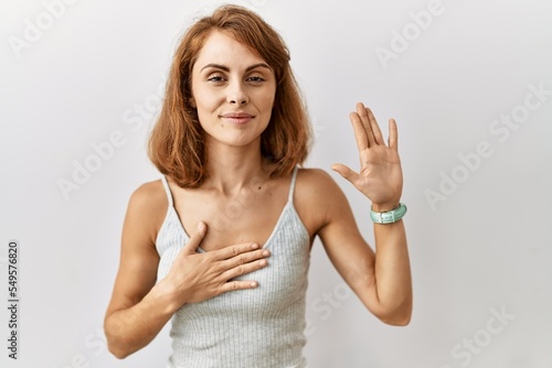Beautiful caucasian woman standing over isolated background swearing with hand on chest and open palm, making a loyalty promise oath