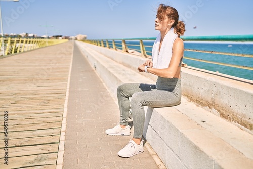 Young caucasian woman wearing sportswear looking watch at seaside