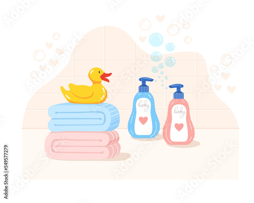 Children's bath accessories on background of tiles and soap bubbles. Baby care. Yellow rubber duck, color towels and shampoo bottles on bathroom countertop.