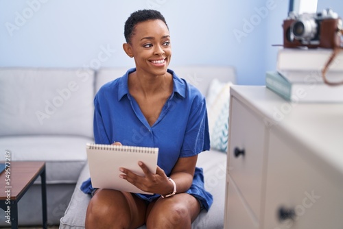 African american woman drawing on notebook sitting on sofa at home