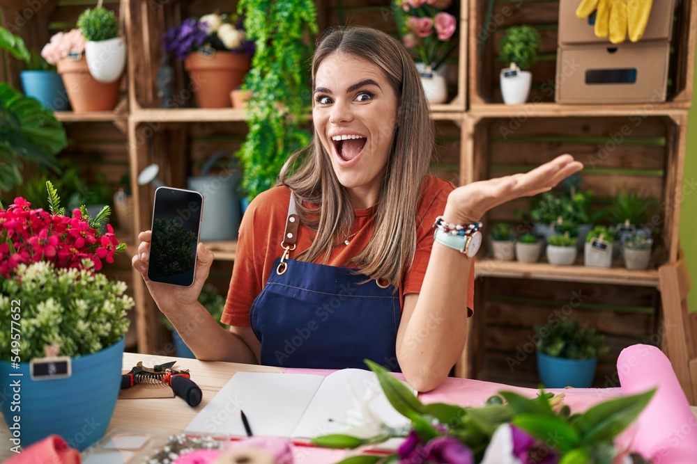 Hispanic young woman working at florist shop showing smartphone screen celebrating victory with happy smile and winner expression with raised hands Hispanic young woman working at florist shop showing smartphone screen celebrating victory with happy smile and winner expression with raised hands