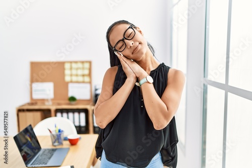 Young hispanic business woman working at the office sleeping tired dreaming and posing with hands together while smiling with closed eyes.
