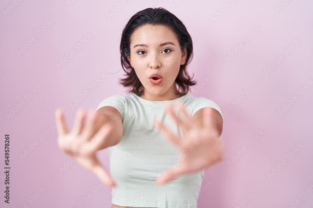 Hispanic young woman standing over pink background doing stop gesture with hands palms, angry and frustration expression Hispanic young woman standing over pink background doing stop gesture with hands palms, angry and frustration expression