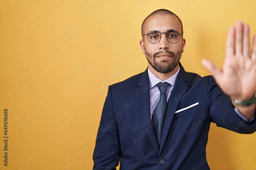 Hispanic man with beard wearing suit and tie doing stop sing with palm of the hand. warning expression with negative and serious gesture on the face. Hispanic man with beard wearing suit and tie doing stop sing with palm of the hand. warning expression with negative and serious gesture on the face.