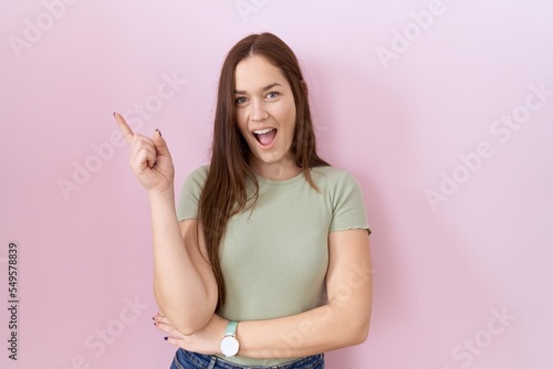 Beautiful brunette woman standing over pink background with a big smile on face, pointing with hand finger to the side looking at the camera. © Krakenimages.com