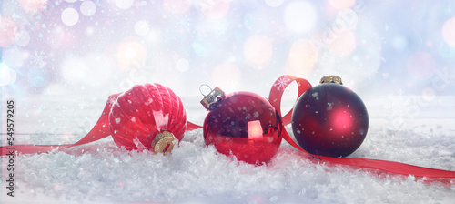 Red Christmas balls with ribbon on snow against blurred lights