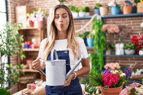 Young blonde woman working at florist shop making fish face with mouth and squinting eyes, crazy and comical.
