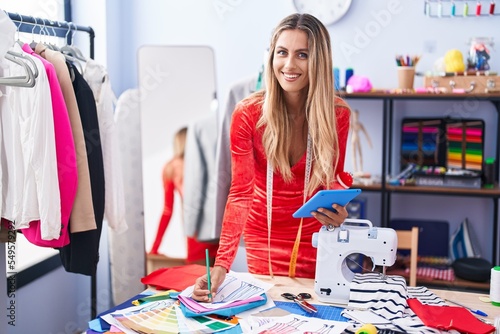 Young blonde woman tailor using touchpad drawing clothing design at tailor shop