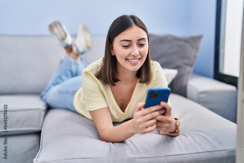Young hispanic woman using smartphone lying on sofa at home Young hispanic woman using smartphone lying on sofa at home