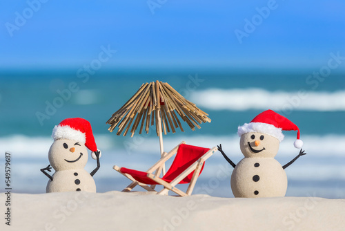 Two Sandy Christmas Snowmen are celebrating Christmas on a beautiful beach, standing next to a sun lounge and a thatched umbrella photo