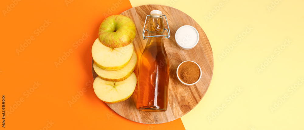 Wooden board with cut apple, bottle of juice, sugar and cinnamon powder on color background, top view