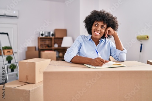 African american woman smiling confident writing on notebook at new home © Krakenimages.com