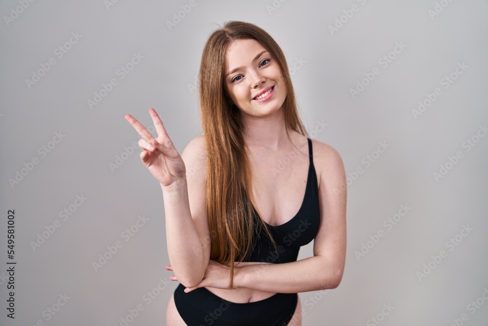 Young caucasian woman wearing lingerie smiling with happy face winking at the camera doing victory sign. number two. Young caucasian woman wearing lingerie smiling with happy face winking at the camera doing victory sign. number two.