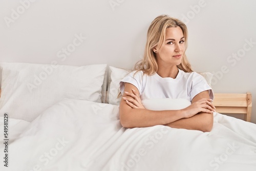Young blonde woman sittin on bed with angry expression at bedroom