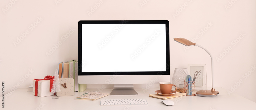 Fototapeta premium Workplace with computer monitor and Christmas gift near light wall