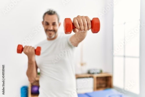 Middle age grey-haired man patient having rehab using dumbbells at rehab clinic