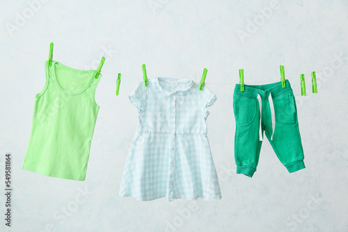 Baby clothes hanging on rope against light background