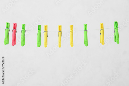 Different plastic clothespins hanging on rope against light background