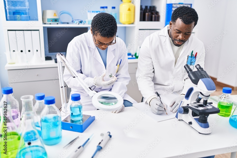 Man and woman scientists writing on notebook working at laboratory Man and woman scientists writing on notebook working at laboratory