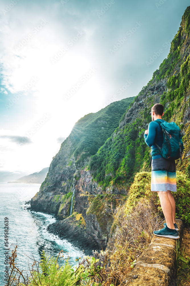 Naklejka premium Sporty man looking at waterfall flowing into the sea in atmospheric morning atmosphere. Viewpoint Véu da Noiva, Madeira Island, Portugal, Europe.