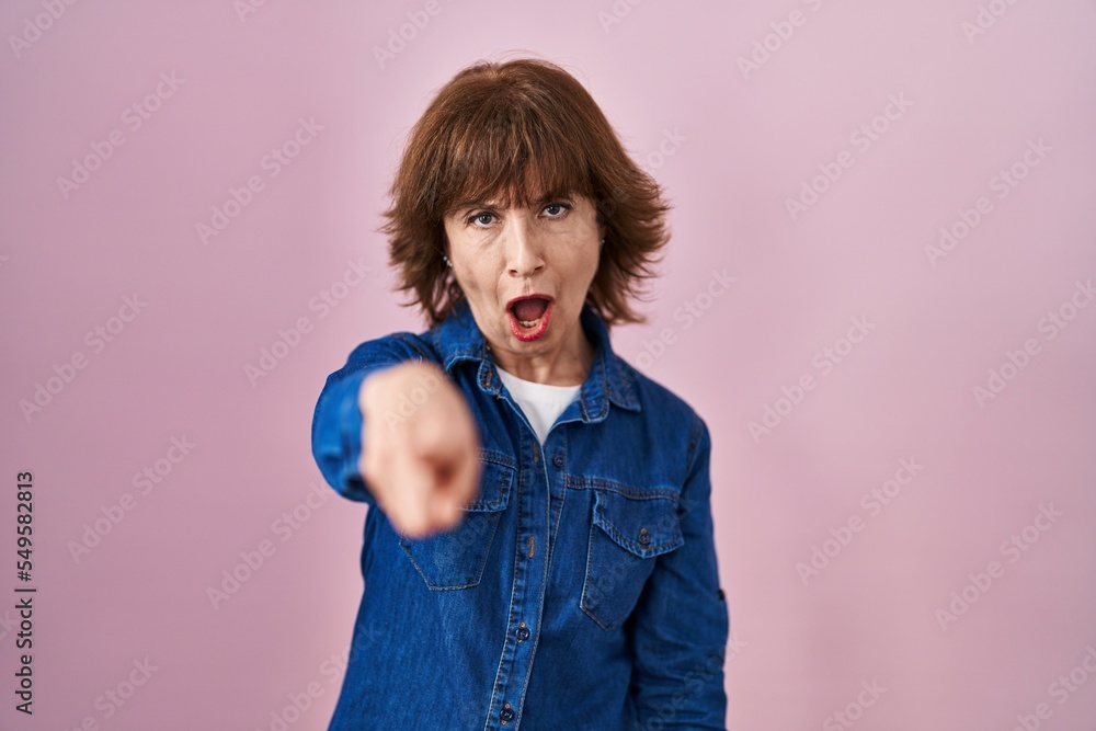 Middle age woman standing over pink background pointing displeased and frustrated to the camera, angry and furious with you Middle age woman standing over pink background pointing displeased and frustrated to the camera, angry and furious with you