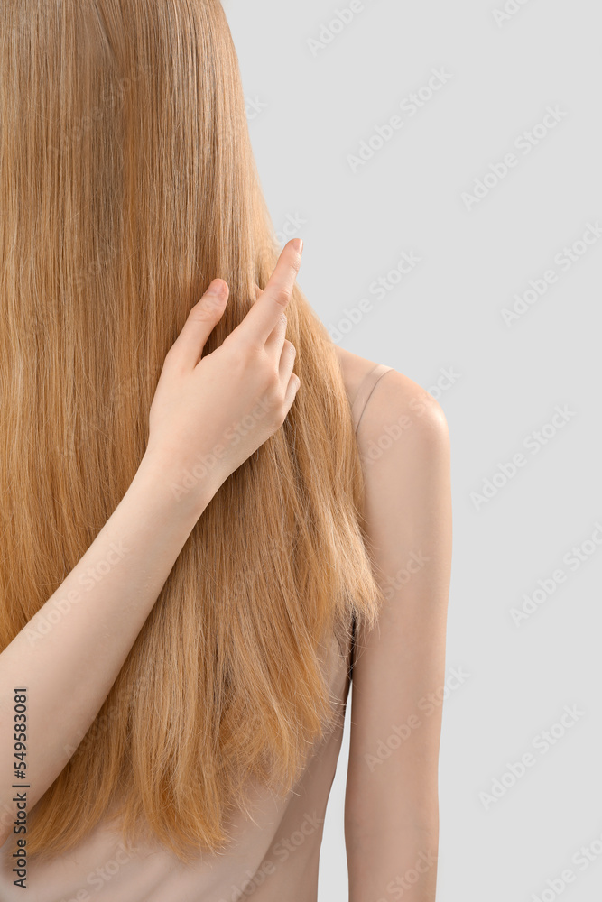 Blonde woman touching long hair on light background, closeup Blonde woman touching long hair on light background, closeup