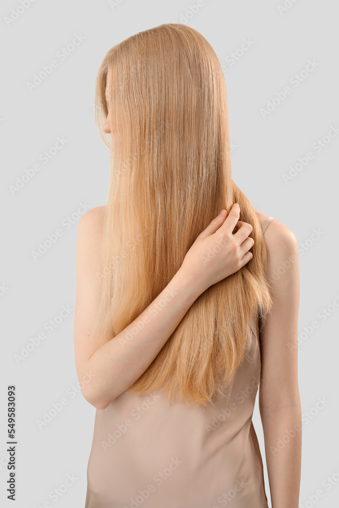Naklejka premium Blonde woman touching long hair on light background