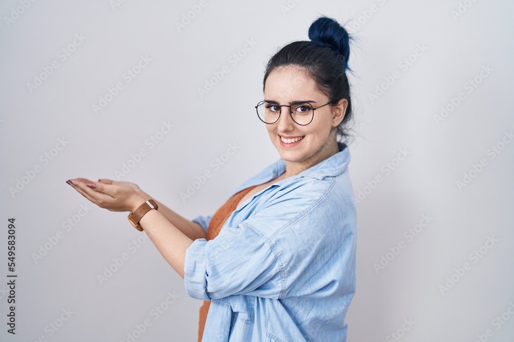 Young modern girl with blue hair standing over white background pointing aside with hands open palms showing copy space, presenting advertisement smiling excited happy Young modern girl with blue hair standing over white background pointing aside with hands open palms showing copy space, presenting advertisement smiling excited happy