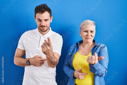 Young brazilian mother and son standing over blue background beckoning come here gesture with hand inviting welcoming happy and smiling