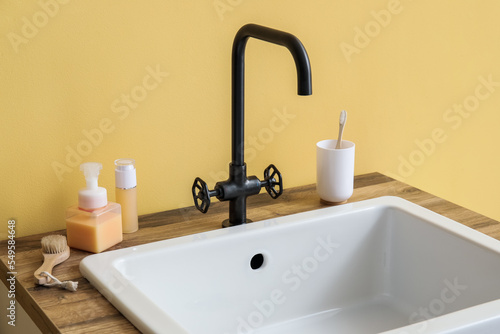 Sink with bath accessories on table near yellow wall