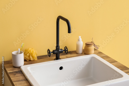 Sink with bath accessories on table near yellow wall