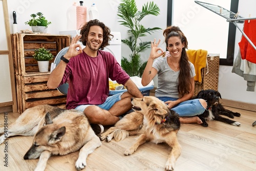 Canvas Print Young hispanic couple doing laundry with dogs smiling positive doing ok sign with hand and fingers