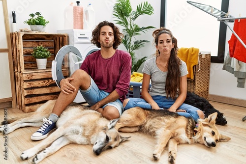 Photography Young hispanic couple doing laundry with dogs looking at the camera blowing a kiss on air being lovely and sexy