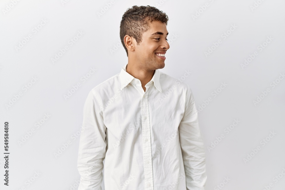 Young handsome hispanic man standing over isolated background looking away to side with smile on face, natural expression. laughing confident. Young handsome hispanic man standing over isolated background looking away to side with smile on face, natural expression. laughing confident.