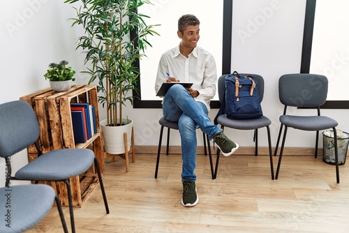 Young hispanic man waiting filling documents on clipboard at waiting room
