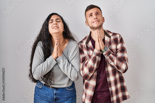 Young hispanic couple standing over white background begging and praying with hands together with hope expression on face very emotional and worried. begging.