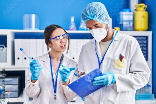 Man and woman scientists holding test tube writing on document at laboratory
