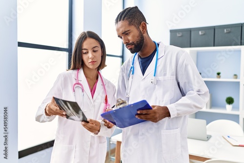 Man and woman wearing doctor uniform looking xray working at clinic