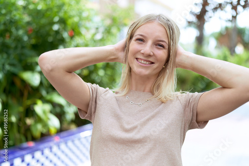 Young blonde woman smiling confident relaxed with hands on head at park