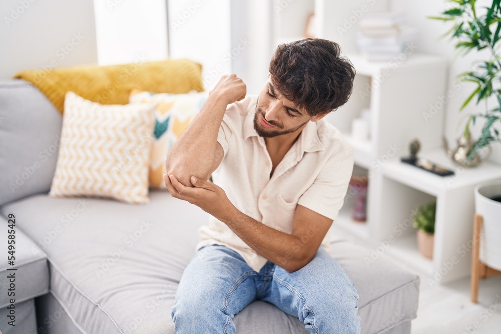 Young arab man suffering for elbow pain sitting on sofa at home Young arab man suffering for elbow pain sitting on sofa at home